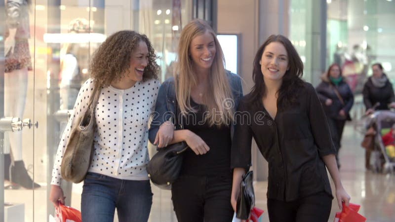 Tre kvinnliga vänner som tillsammans shoppar i galleria