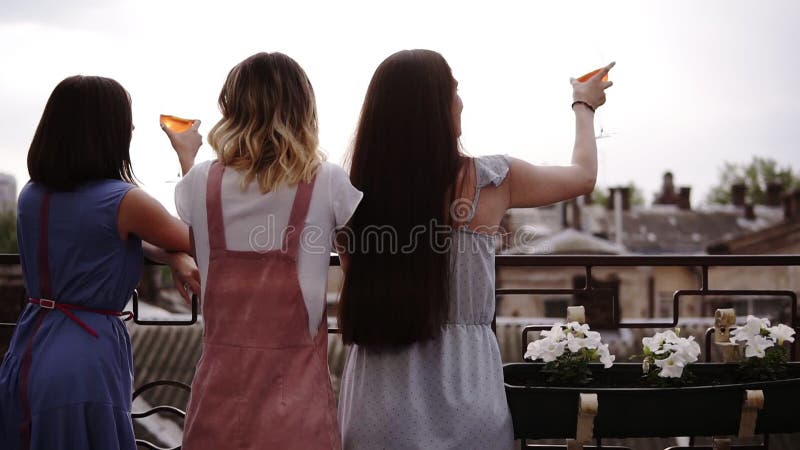 Tre kvinnliga vänner som tycker om möhippan på terrassen, baksikt Infall modern kläder Härlig stadssikt på