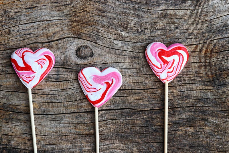 Tre lecca-lecca rosse nel cuore modellano su fondo di legno fotografia stock Tre lecca-lecca rosse nel cuore modellano su fondo di legno fotografia stock