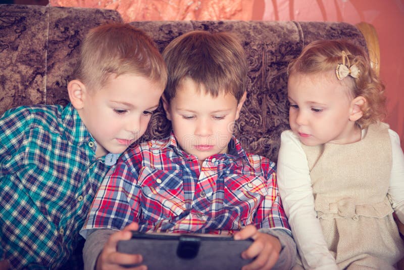 Tre lilla barn som spelar med minnestavlaPC royaltyfri bild Tre lilla barn som spelar med minnestavlaPC royaltyfri bild
