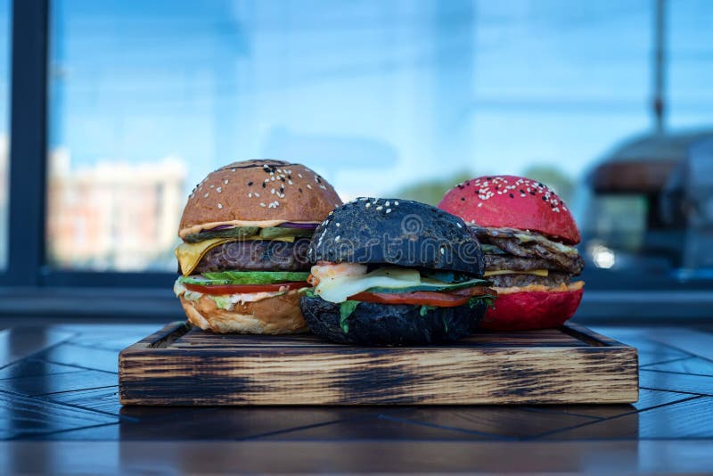 Tre olika hamburgare på träbräde royaltyfria bilder Tre olika hamburgare på träbräde royaltyfria bilder
