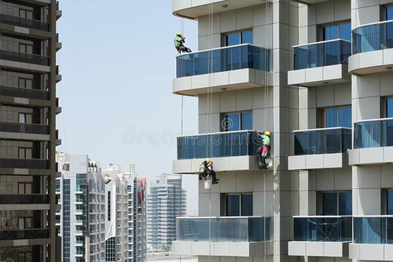 Tre operai di alto livello lavano i vetri di un edificio a sviluppo verticale fotografia stock libera da diritti