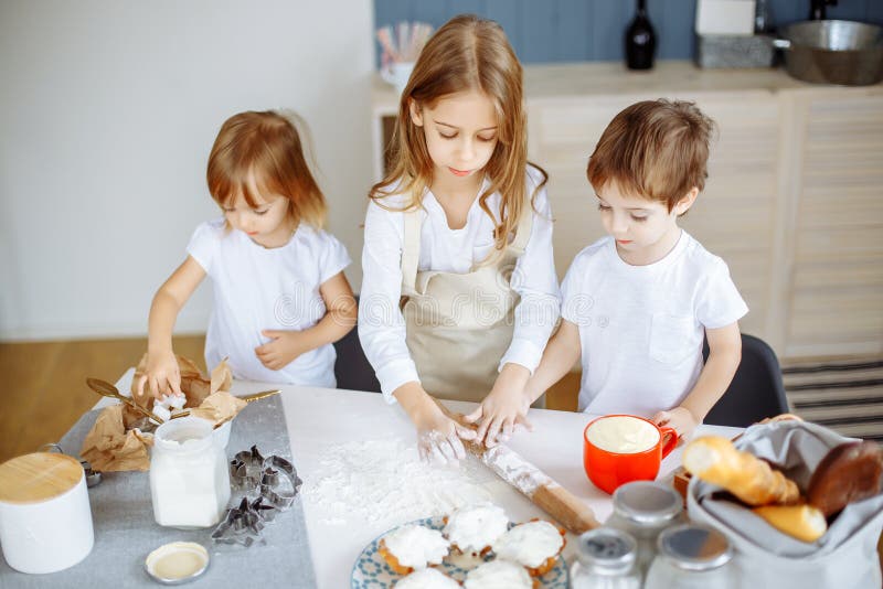 Tre piccoli cuochi unici che godono nella cucina che fa grande mess Bambini che producono i biscotti nella cucina fotografie stock libere da diritti Tre piccoli cuochi unici che godono nella cucina che fa grande mess Bambini che producono i biscotti nella cucina fotografie stock libere da diritti