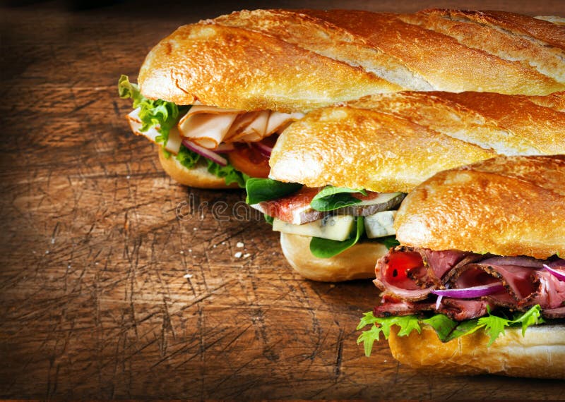 Three tasty baguettes with savory fillings lined up on a rustic wooden countertop with roast beef and rocket, figs and cheese, and chicken and salad fillings. Three tasty baguettes with savory fillings lined up on a rustic wooden countertop with roast beef and rocket, figs and cheese, and chicken and salad fillings