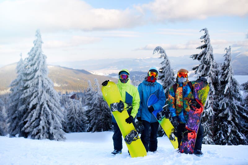 Tre snowboarders som poserar på, skidar semesterorten Vänner som klättrar till bergöverkanten som bär deras snowboards till och m fotografering för bildbyråer Tre snowboarders som poserar på, skidar semesterorten Vänner som klättrar till bergöverkanten som bär deras snowboards till och m fotografering för bildbyråer