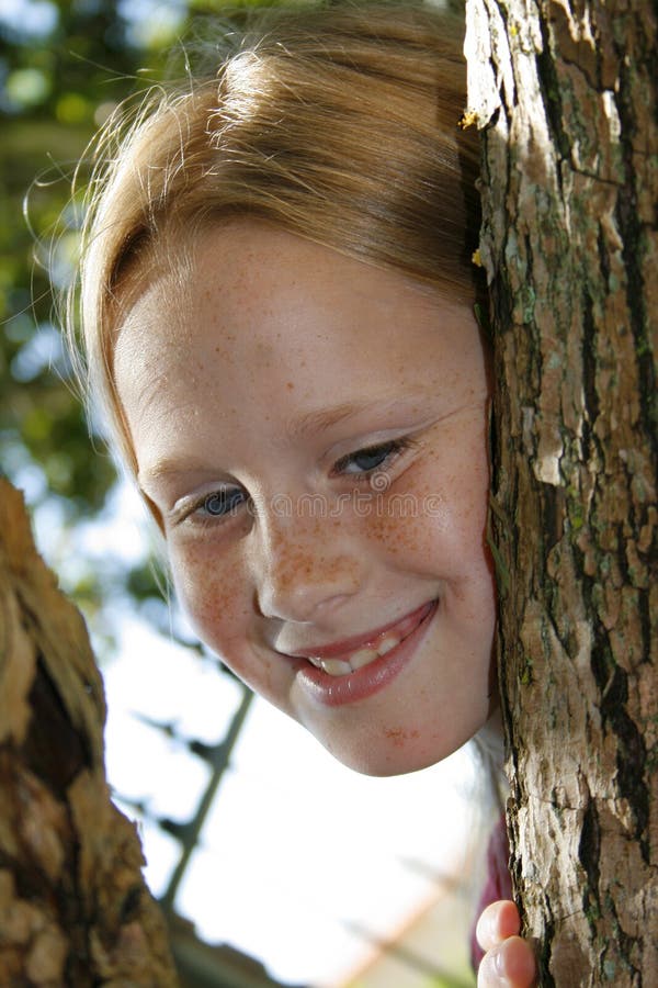 A portrait of a beautiful blond child peeking through the branches of a tree. A portrait of a beautiful blond child peeking through the branches of a tree