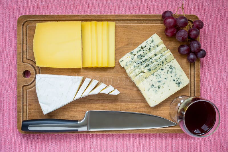 Tree kind of sliced cheese, glass of red wine, sweet red grapes and chef knife on brown wooden cutting board. cheese with edible royalty free stock photography Tree kind of sliced cheese, glass of red wine, sweet red grapes and chef knife on brown wooden cutting board. cheese with edible royalty free stock photography