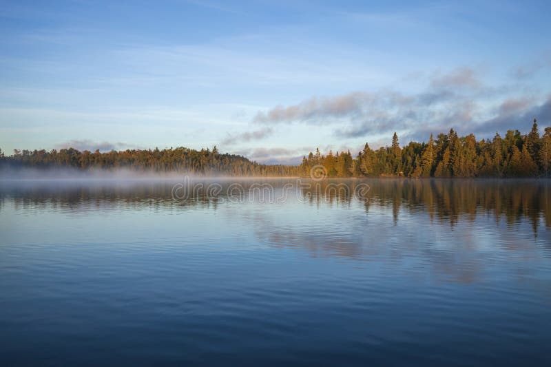 Trees and shoreline in early morning fog and light on a beautiful blue northern Minnesota lake in September