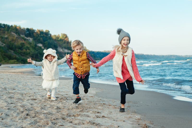 Trei copii albi și zâmbitori, glumeți, prieteni, care se joacă pe plajă pe plajă, la apus stock images