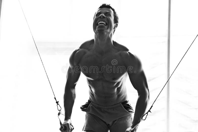 Artistic shot, black and white, of a young bodybuilder hard taining in the gym: cable crossover. Artistic shot, black and white, of a young bodybuilder hard taining in the gym: cable crossover