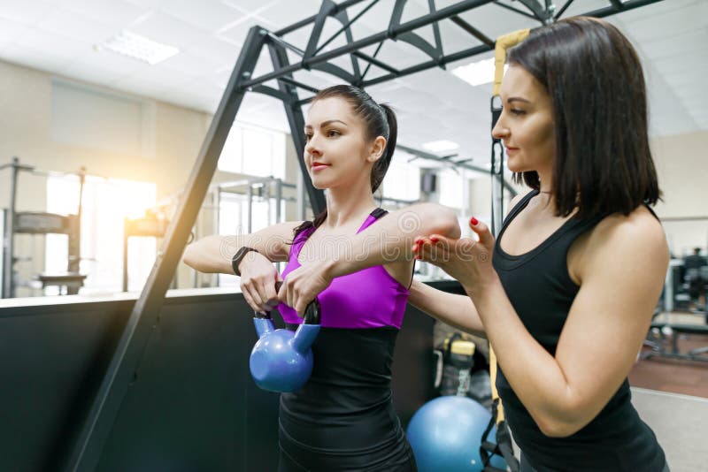 Treinamento pessoal do instrutor da aptidão e mulher de ajuda do cliente que fazem o exercício com peso no gym Aptidão, esporte