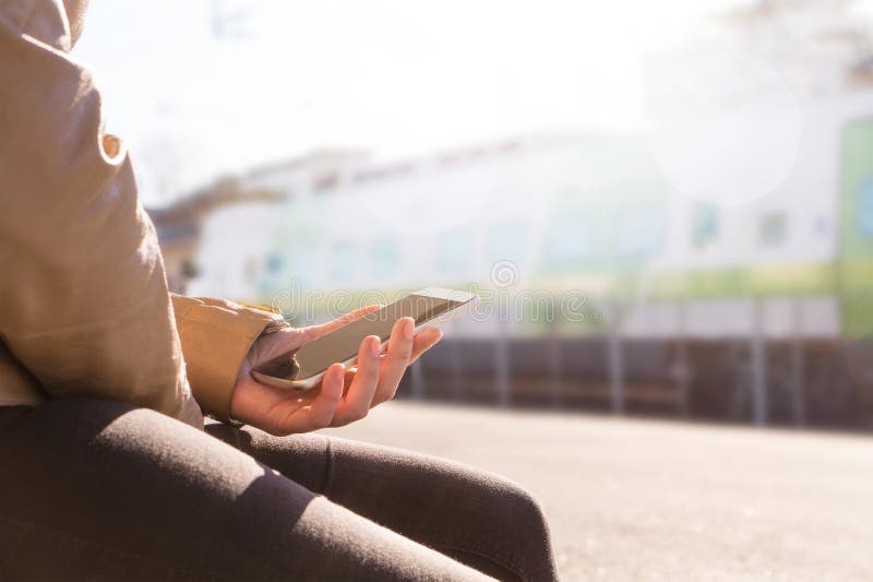 Trem de espera da mulher na plataforma e no smartphone da utilização para comprar o bilhete eletrónico ou a programação da consul foto de stock Trem de espera da mulher na plataforma e no smartphone da utilização para comprar o bilhete eletrónico ou a programação da consul foto de stock