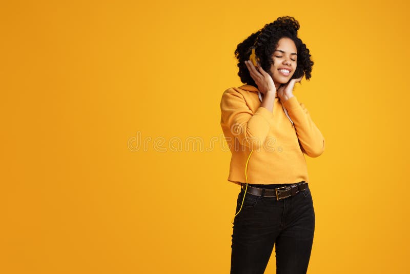 Trendy african american young woman with bright smile dressed in casual clothes and headphones clothing listening music stock photos Trendy african american young woman with bright smile dressed in casual clothes and headphones clothing listening music stock photos