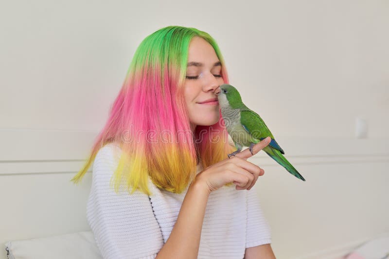 Trendy with colored hair teenager girl with green parrot on hand