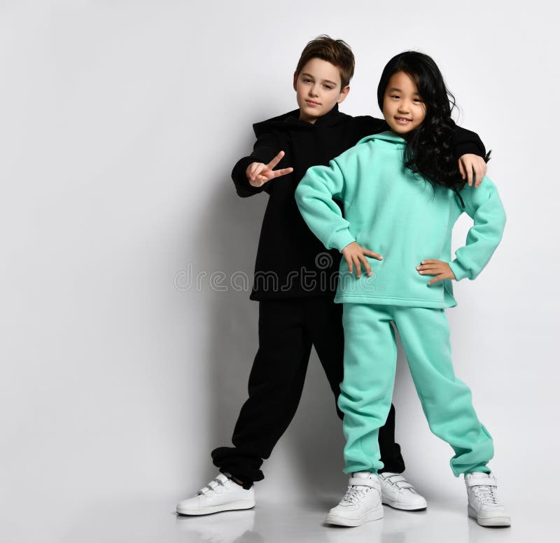 Fashionable interracial sports boy and girl in warm sportswear standing together. Full length portrait of Caucasian men hugging female Asian child. Friendship, children& x27;s fashion. Fashionable interracial sports boy and girl in warm sportswear standing together. Full length portrait of Caucasian men hugging female Asian child. Friendship, children& x27;s fashion