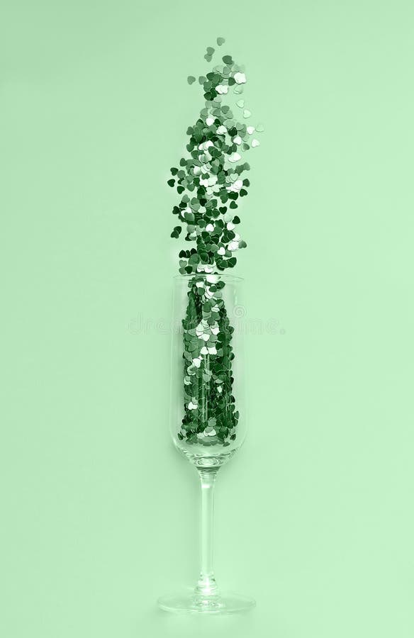 Trendy neo mint heart-shaped confetti poured out of champagne glass. Flat lay. Love and celebration concept.