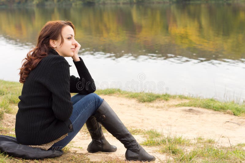 Trendy young woman sitting on a river bank