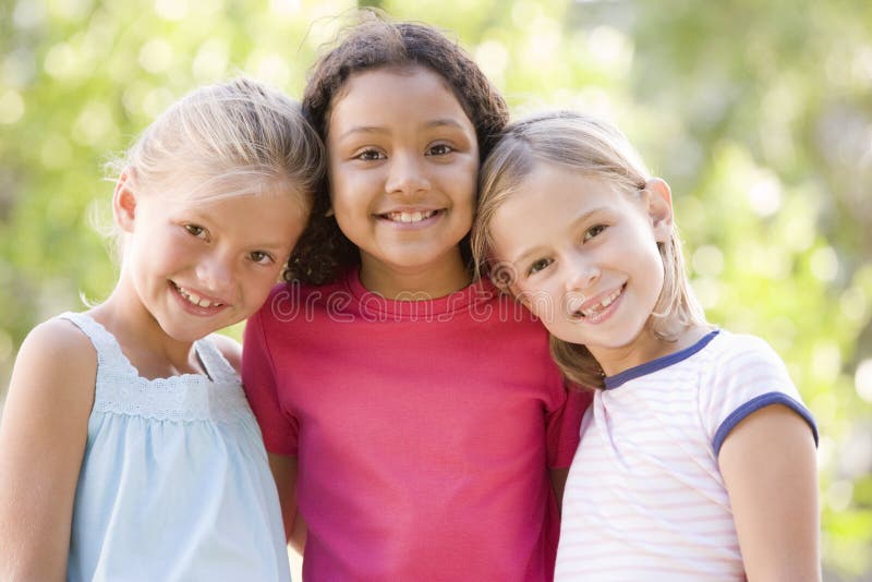 Tres amigos de la chica joven que se colocan al aire libre sonrientes imagen de archivo