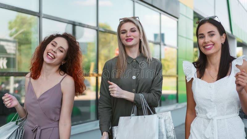 Tres bonitas compradoras sonrientes bailando al aire libre en el fondo de una vidriera almacen de metraje de vídeo