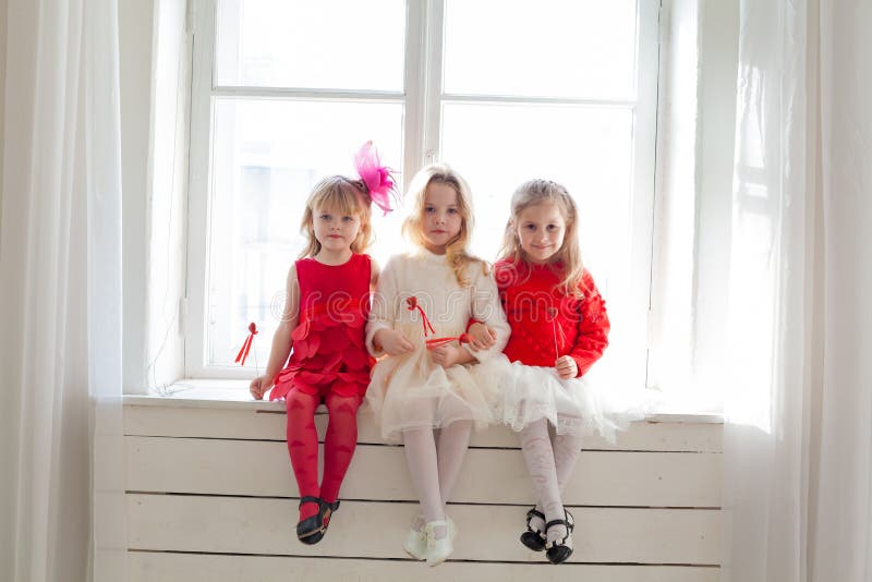 Tres chicas con vestidos rojos blancos sentadas junto a la ventana foto de archivo Tres chicas con vestidos rojos blancos sentadas junto a la ventana foto de archivo