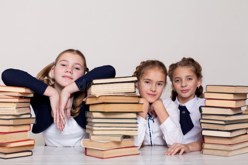Tres colegialas de las muchachas en un escritorio con los libros en la lección en la escuela fotos de archivo libres de regalías Tres colegialas de las muchachas en un escritorio con los libros en la lección en la escuela fotos de archivo libres de regalías