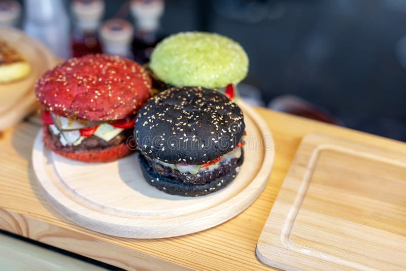 Tres hamburguesas multicoloras brillantes sabrosas de la carne de vaca en contador de madera en el bollo del amburger del fest de imágenes de archivo libres de regalías Tres hamburguesas multicoloras brillantes sabrosas de la carne de vaca en contador de madera en el bollo del amburger del fest de imágenes de archivo libres de regalías