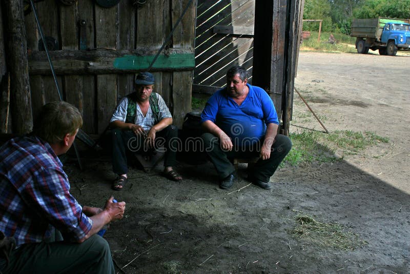 Tres hombres, trabajadores de granja que hablan en sombra del granero de madera fotografía de archivo libre de regalías Tres hombres, trabajadores de granja que hablan en sombra del granero de madera fotografía de archivo libre de regalías