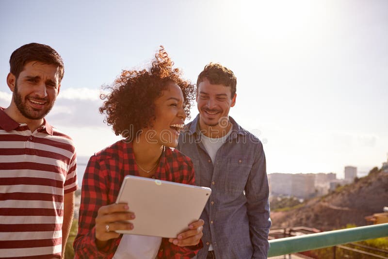 Tres millennials de risa con una tableta fotografía de archivo libre de regalías Tres millennials de risa con una tableta fotografía de archivo libre de regalías