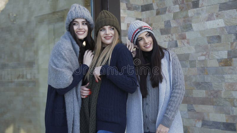 Tres muchachas bonitas en los casquillos y la bufanda que presentan en la yarda almacen de video