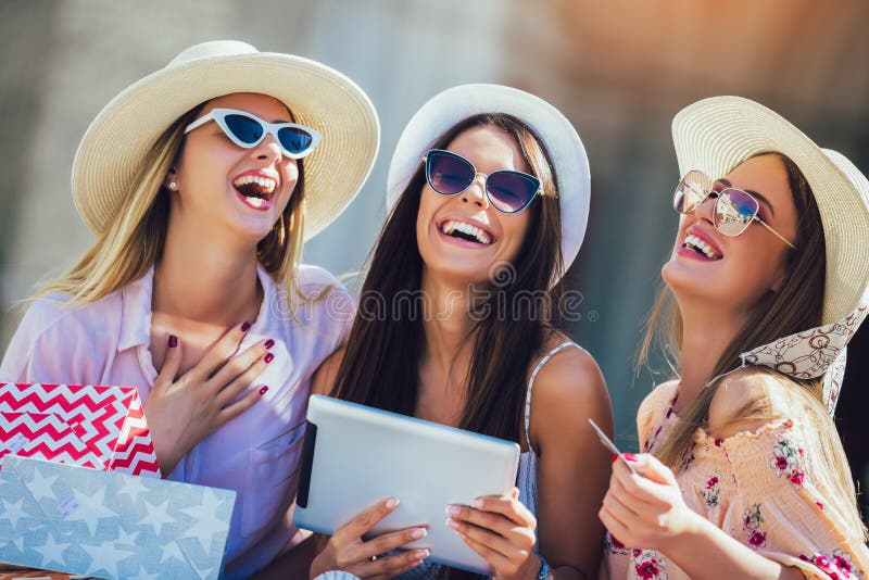 Tres muchachas con los bolsos que hacen compras coloridos usando la tarjeta digital de la tableta y de crédito al aire libre