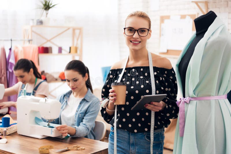 Tres muchachas en la fábrica de la ropa Se están sentando detrás de las máquinas de coser y están mirando diseño de nuevo vestido fotos de archivo Tres muchachas en la fábrica de la ropa Se están sentando detrás de las máquinas de coser y están mirando diseño de nuevo vestido fotos de archivo