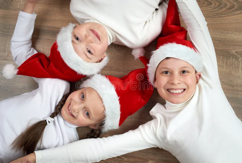 Tres niños en los sombreros de Papá Noel que mienten en fondo de madera, teniendo la diversión y emociones felices, concepto de l fotos de archivo Tres niños en los sombreros de Papá Noel que mienten en fondo de madera, teniendo la diversión y emociones felices, concepto de l fotos de archivo