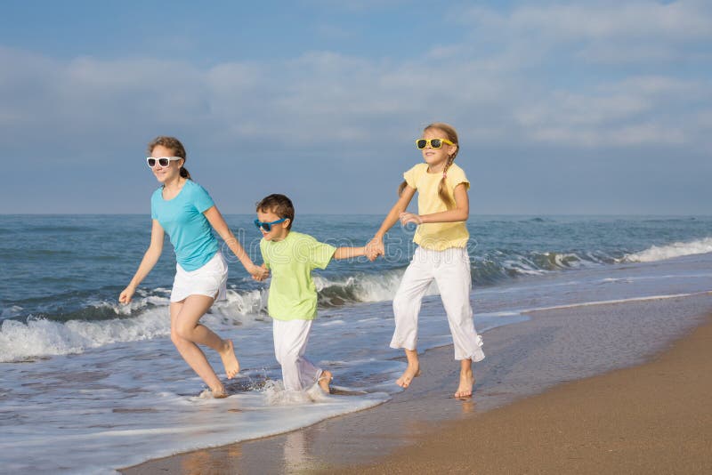 Tres niños felices que corren en la playa en el tiempo del día fotografía de archivo libre de regalías Tres niños felices que corren en la playa en el tiempo del día fotografía de archivo libre de regalías