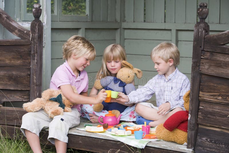 Three young children in shed playing tea and smiling. Three young children in shed playing tea and smiling
