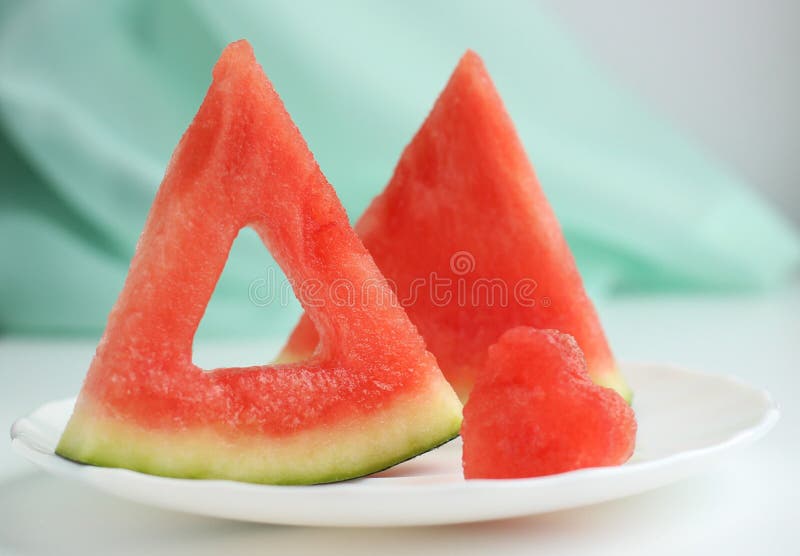 Triangular pieces of watermelon with a heart cut from the pulp of watermelon in a cup on a light background. High quality photo. Triangular cut watermelon stock images, royalty-free photos and pictures