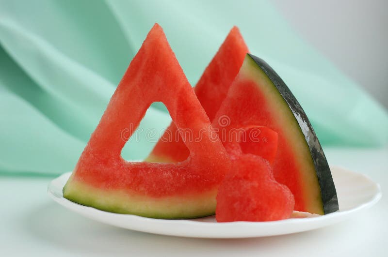 Triangular pieces of watermelon with a heart cut from the pulp of watermelon in a cup on a light background. High quality photo. Triangular cut watermelon stock images, royalty-free photos and pictures