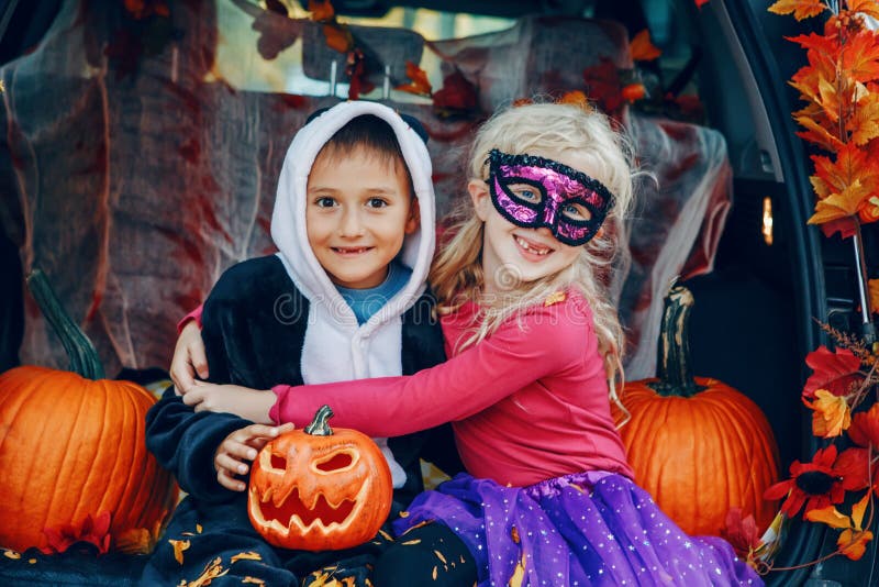 Trick oder Stamm Kinder, die Halloween im Stamm des Autos feiern. Junge und Mädchen mit roten Kürbisen traditionelle Oktober feie