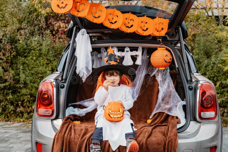 Trick oder Stamm. Stamm oder Leckerbissen. wenig Kind im Hexenhut Halloween-Partei in verziertem Stamm des Autos feiern