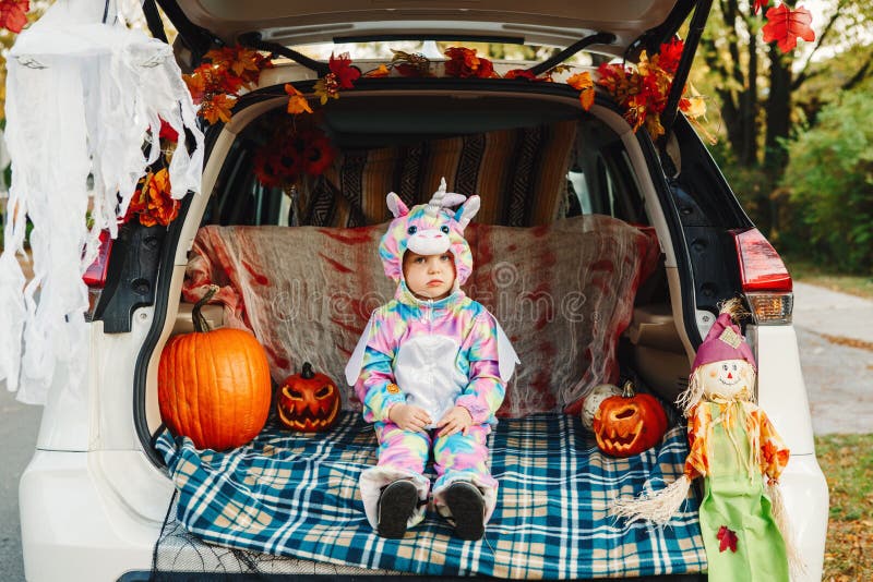 Trick or trunk. Sad upset baby in unicorn costume celebrating Halloween in trunk of car. Cute toddler celebrating October holiday