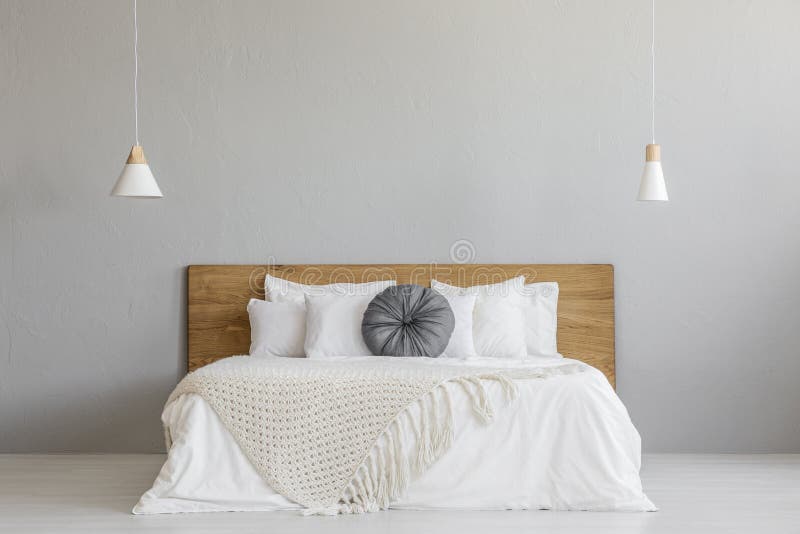 Knit blanket on wooden bed against grey wall in minimal bedroom interior with lamps. Real photo with a place for your nightstand. Knit blanket on wooden bed against grey wall in minimal bedroom interior with lamps. Real photo with a place for your nightstand