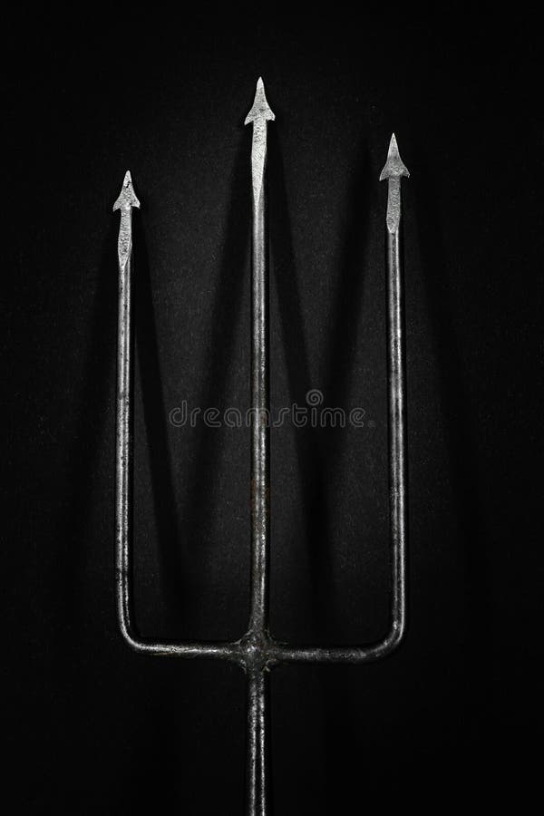 Tridente velho, oxidado e do metal que molda a sombra na superfície preta do fundo fotografia de stock Tridente velho, oxidado e do metal que molda a sombra na superfície preta do fundo fotografia de stock
