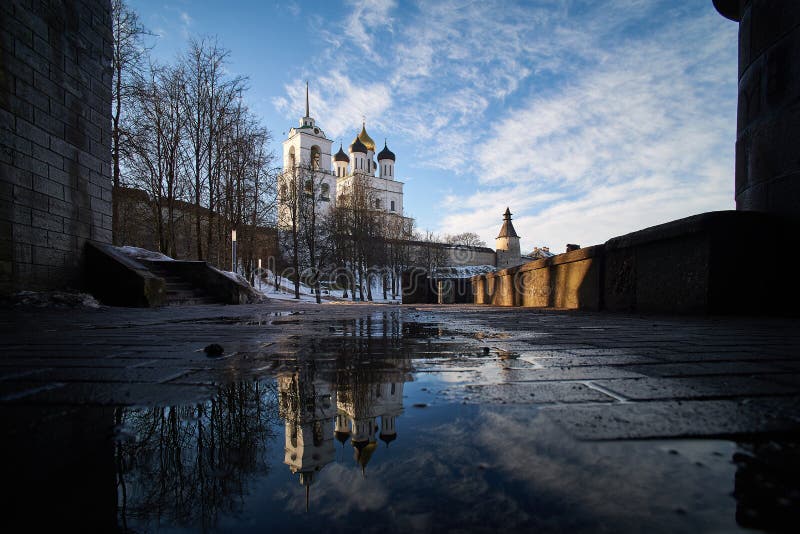Horizontal shot of Trinity Cathedral in Pskov kremlin with reflection in the water of a spring puddle.