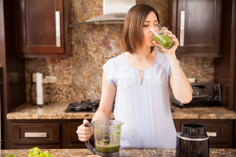 Young woman drinking some green and healthy juice she just made in a blender at home. Young woman drinking some green and healthy juice she just made in a blender at home