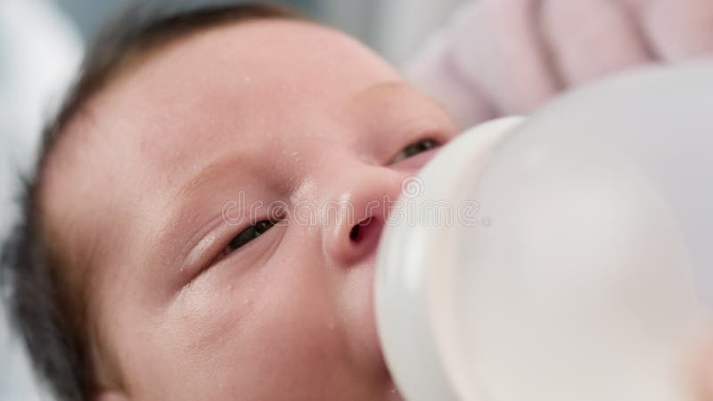 Trinkende Muttermilch des Kaukasus Neugeborenen von der kleinen Plastikbabyflasche durch Friedensschaffung. Porträtkleinkindtrinke