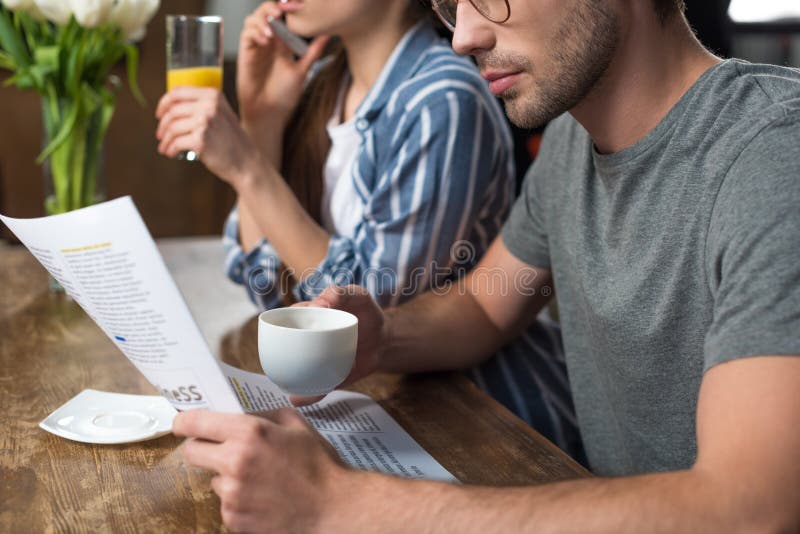 Trinkender Saft der jungen Frau, der am Telefon während trinkender Kaffee des Mannes spricht lizenzfreies stockbild