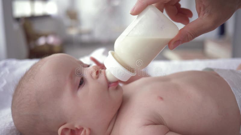 Trinkmilch des neugeborenen Babys von einer Flasche dass Muttergriffe in ihren Händen, Porträt wenigen Mädchens in der Windel auf