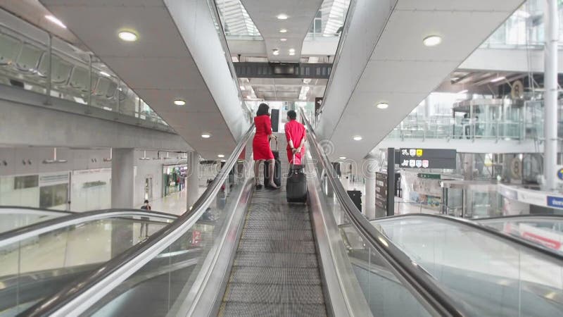 Tripulações de cabina, de uniforme vermelho, que utilizam escadas rolantes no terminal aeroportuário.