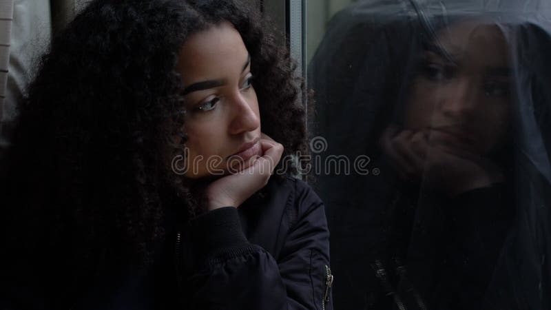Triste déprimée belle métisse afro-américaine adolescente regardant par la fenêtre banque de vidéos