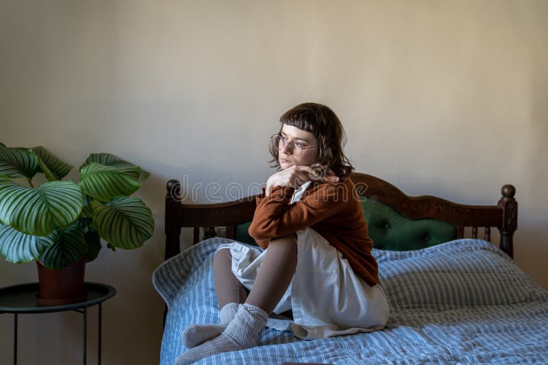 Triste femme mélancolique assise toute seule sur son lit regardant par la fenêtre. sensation de solitude mélancolie automnale photos stock