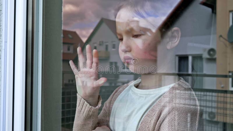 Triste petite fille regarde par la fenêtre pressant sa paume contre le verre. clips vidéos